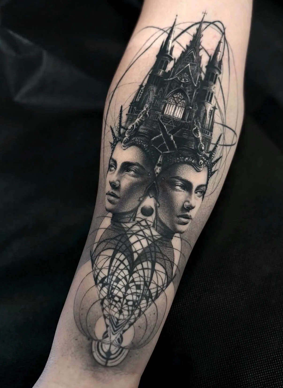 Zwei gekrönte Frauengesichter, aus denen eine gotische Kathedrale wächst, darunter geometrische Kreise. Black-and-Grey-Tattoo von Sloan auf dem Unterarm.