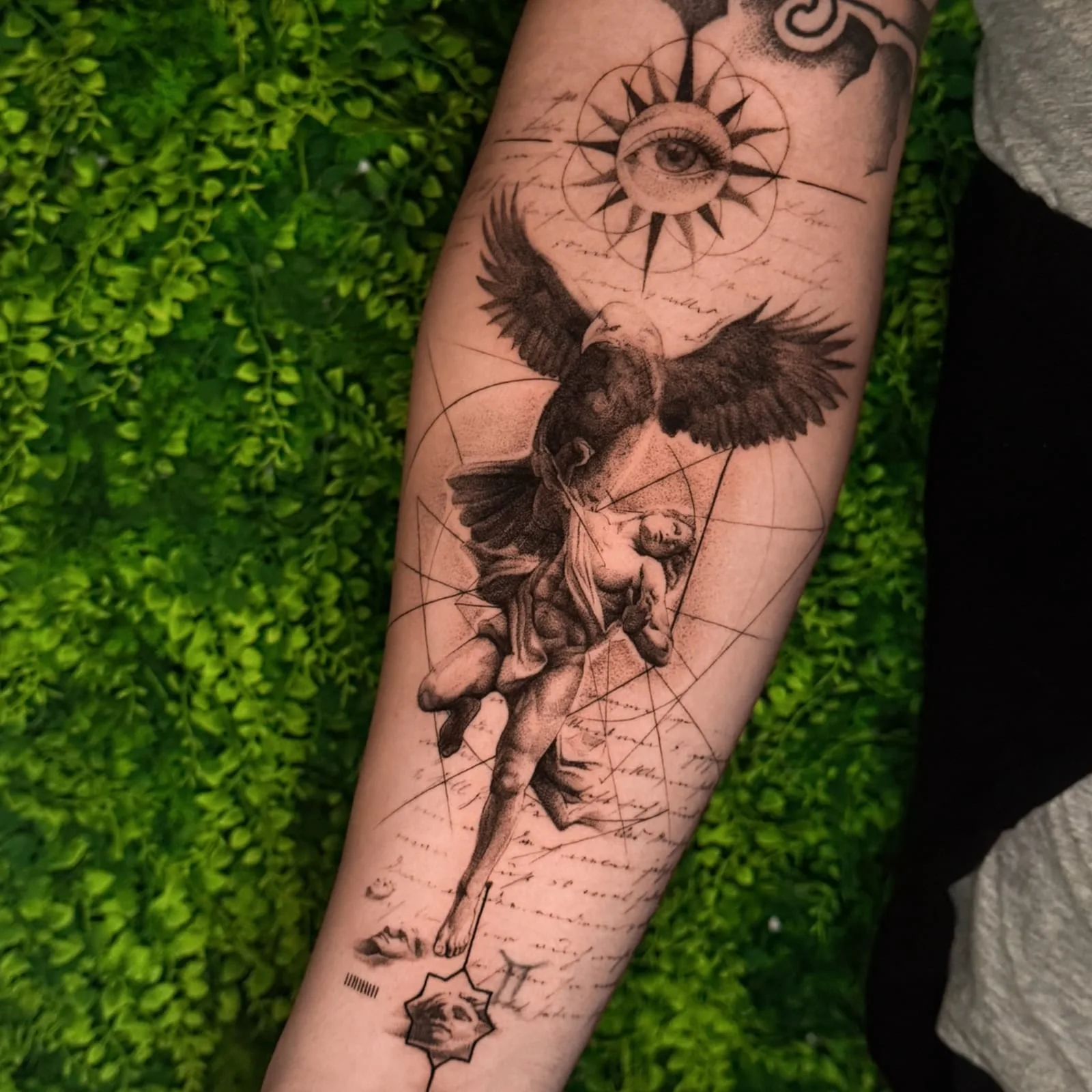 Ein Adler trägt einen Engel nach oben, darüber eine Sonne mit Auge, dazu Handschrift und feine Linien. Black-and-Grey-Tattoo von Inna auf dem Unterarm.