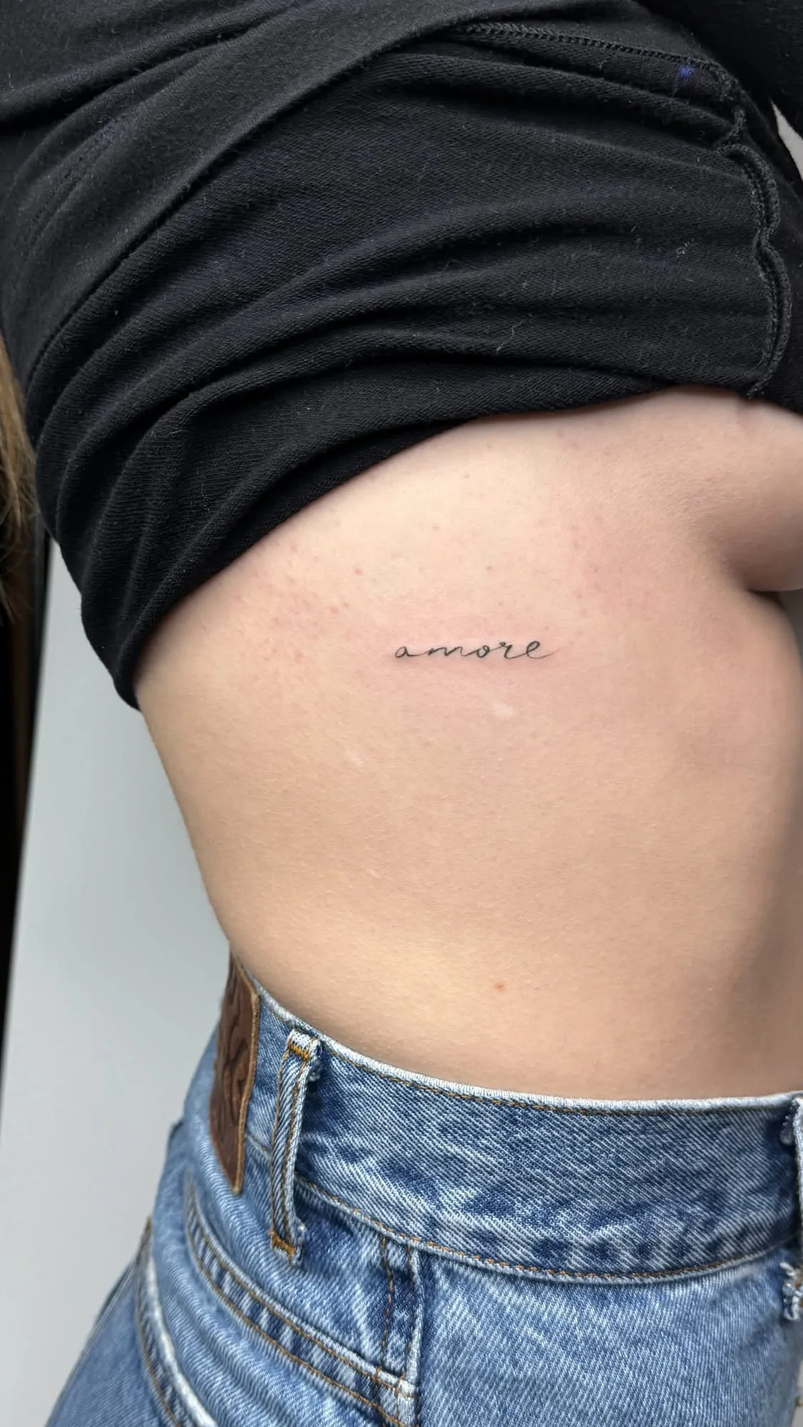 Der Schriftzug Amore in feiner Handschrift. Fine-Line-Tattoo von Inna an der Rippe.
