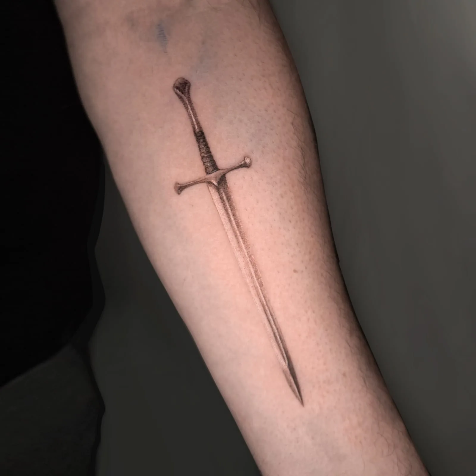 Langes Schwert mit umwickeltem Griff, fein schattiert. Fine-Line-Tattoo von Inna auf dem Unterarm.