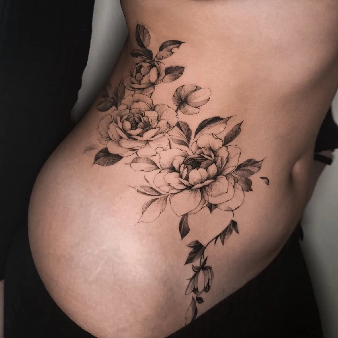 Pfingstrosen mit Blättern und Knospen, fein schattiert. Fine-Line-Tattoo von Inna an der Rippe.