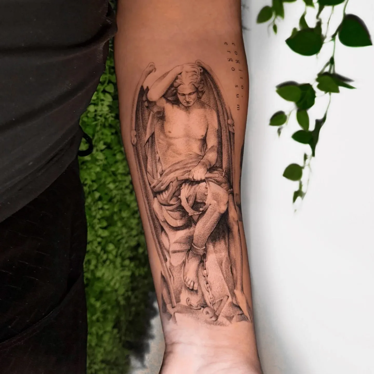 Gefallener Engel nach einer Marmorstatue, mit gesenktem Kopf und Flügeln. Black-and-Grey-Tattoo von Inna auf dem Unterarm.