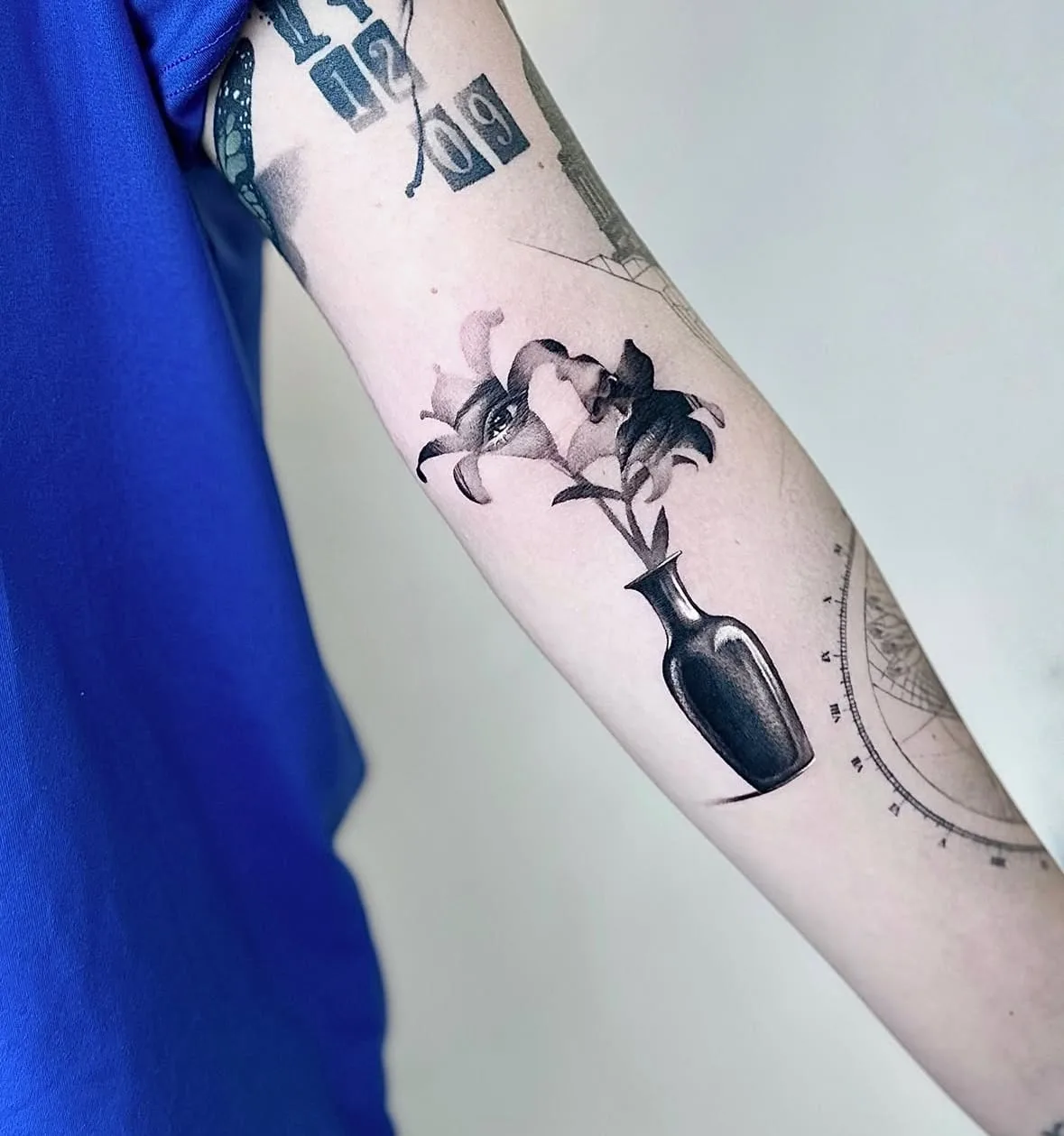 Vase mit zwei Lilien, in einer Blüte ein Auge. Black-and-Grey-Tattoo von Sloan auf dem Arm.