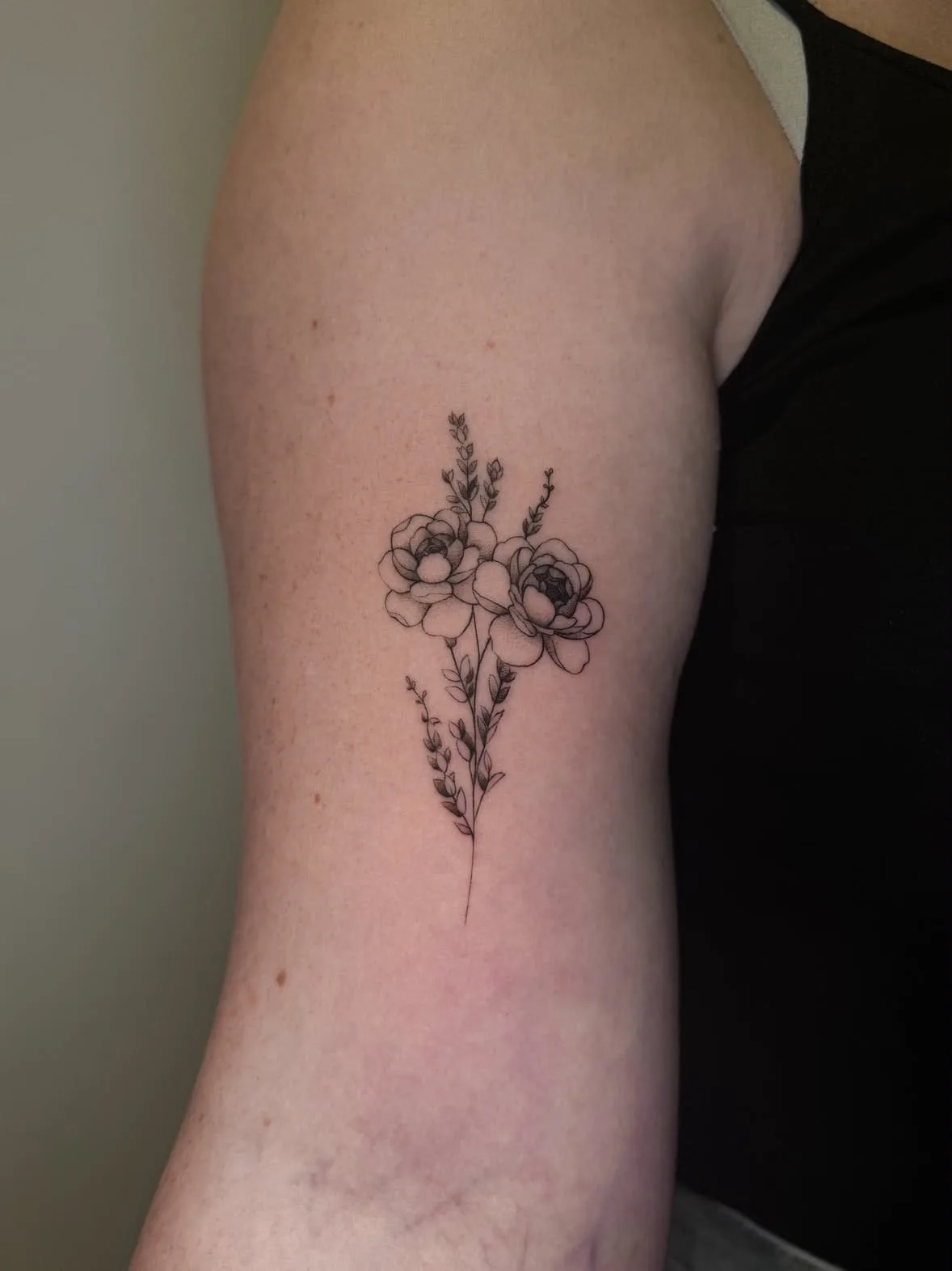 Zwei Blüten mit feinen Stielen und Lavendel. Fine-Line-Tattoo von Inna am Oberarm.