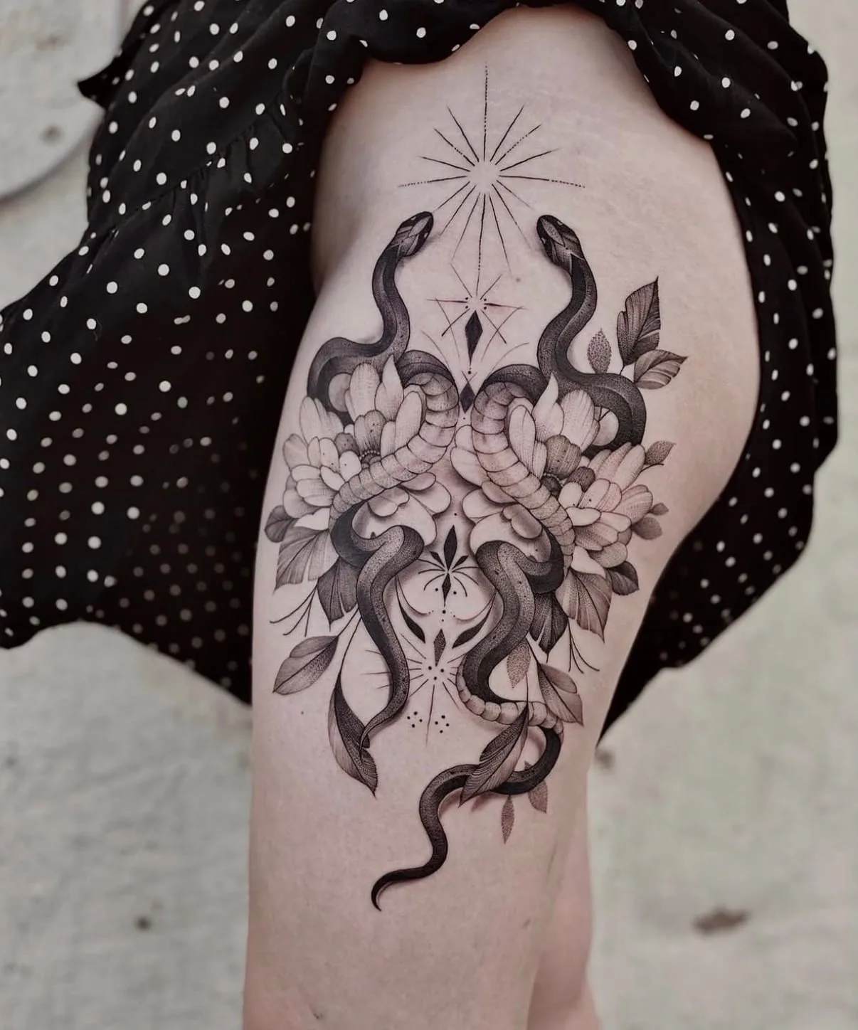 Zwei Schlangen zwischen Pfingstrosen, darüber ein Stern aus feinen Linien, auf dem Oberschenkel. Fine-Line-Tattoo in Black & Grey von Annlie.