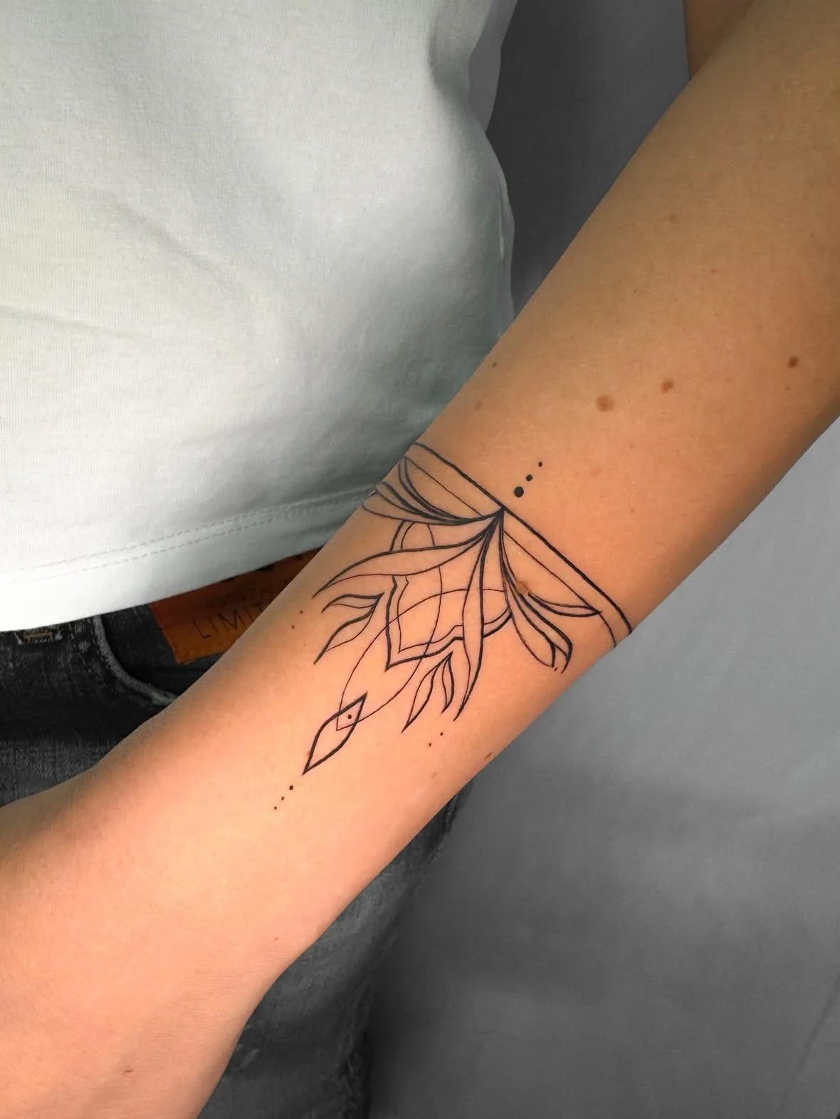 Band um den Arm mit Blättern und feinem Ornament. Fine-Line-Tattoo von Inna am Unterarm.