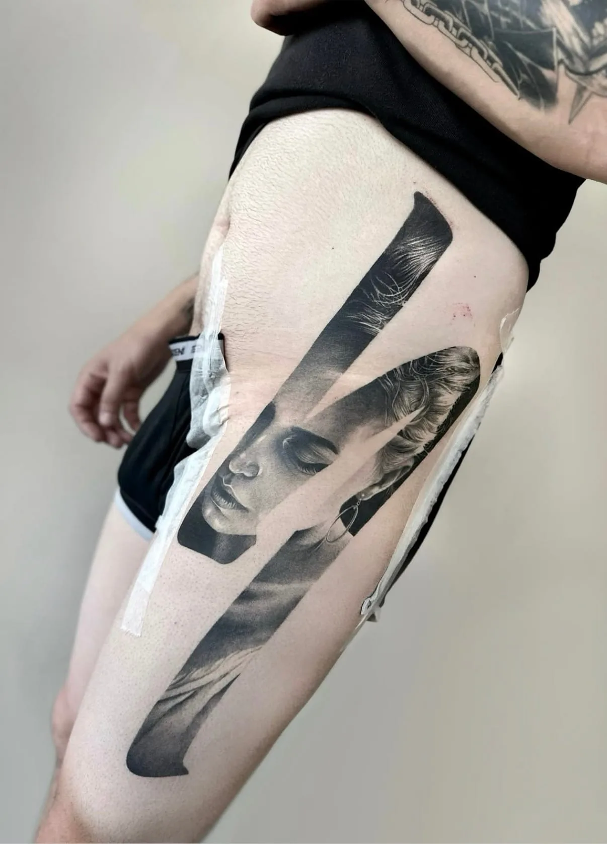 Frauengesicht mit geschlossenen Augen, sichtbar in breiten schrägen Streifen. Black-and-Grey-Tattoo von Sloan auf dem Oberschenkel.