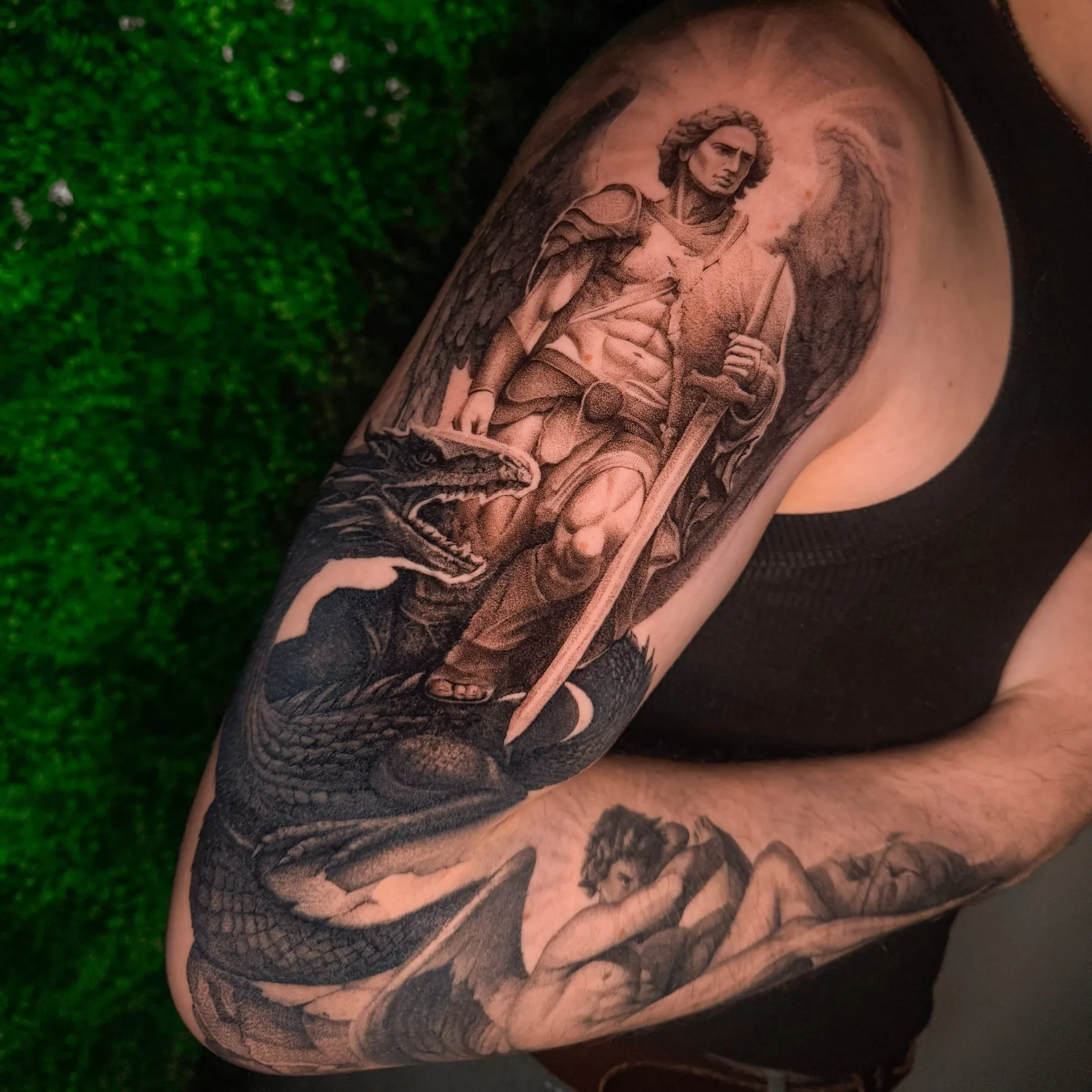 Erzengel Michael mit Schwert über einem Drachen, als großes Motiv über Schulter und Oberarm. Black-and-Grey-Tattoo von Inna.