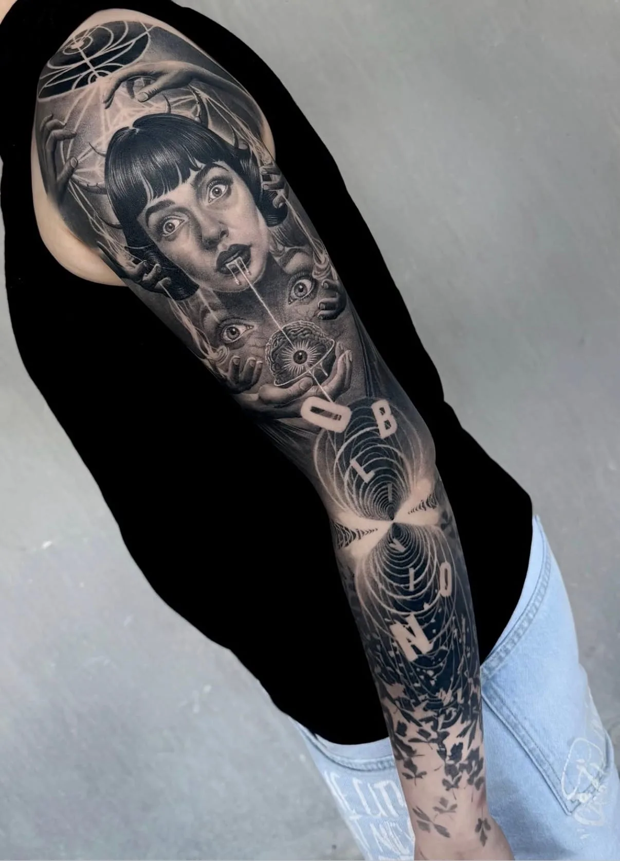 Black-and-Grey-Sleeve von Sloan über den ganzen Arm: Frauengesicht mit Hörnern, Hände und Augen, darunter der Schriftzug OBLIVION in Spiralen.
